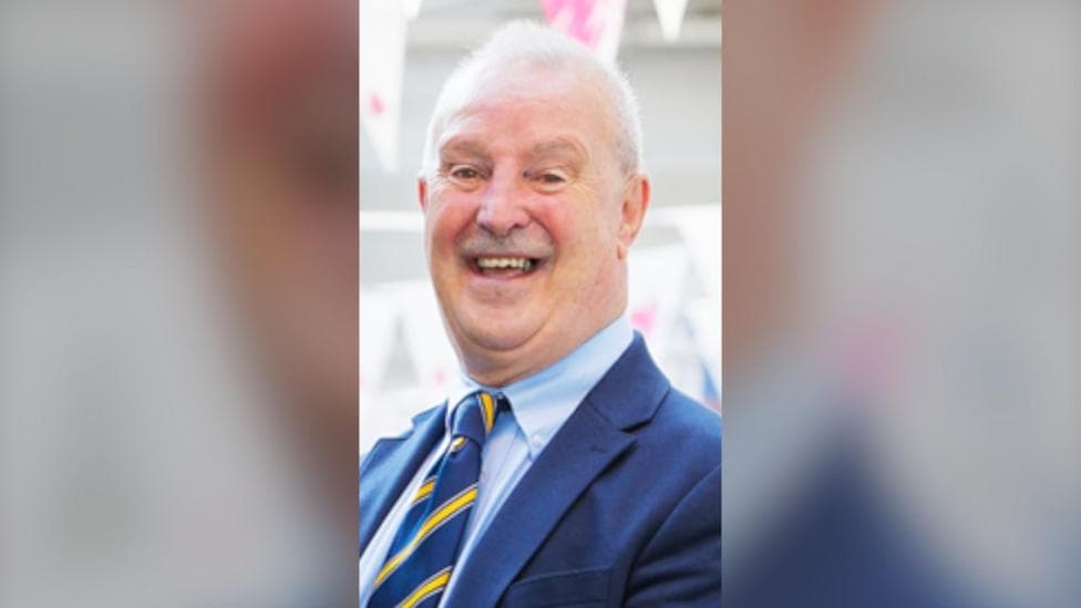 Steve Hunt, a man in a navy suit smiling wearing a blue tie with yellow stripes. He has short white hair and is clean shaven.