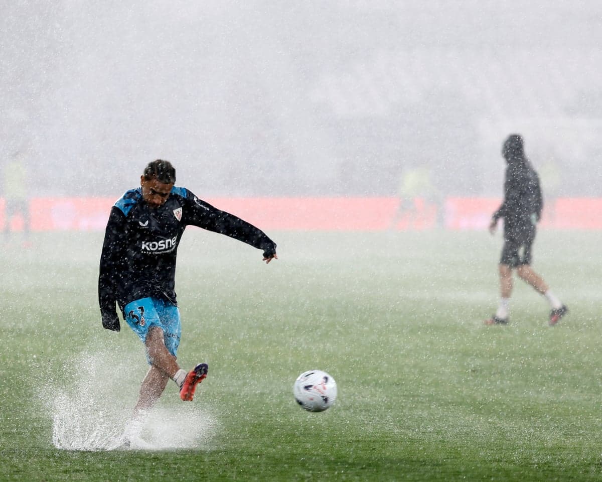 An Athletic Club soccer player kicks a ball on flooded pitch during a rainy warm-up session