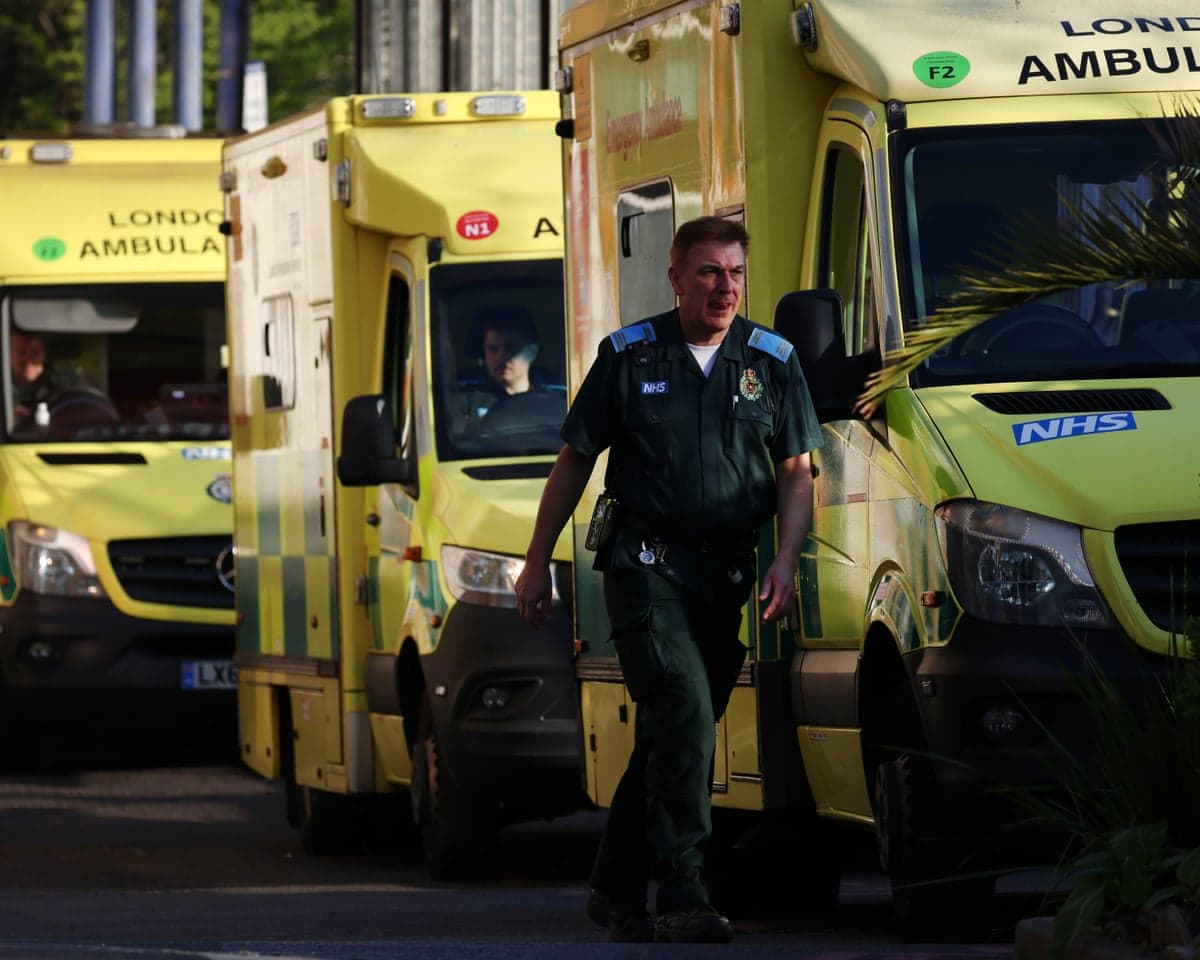 An NHS ambulance worker walks past parked yellow London Ambulance vehicles
