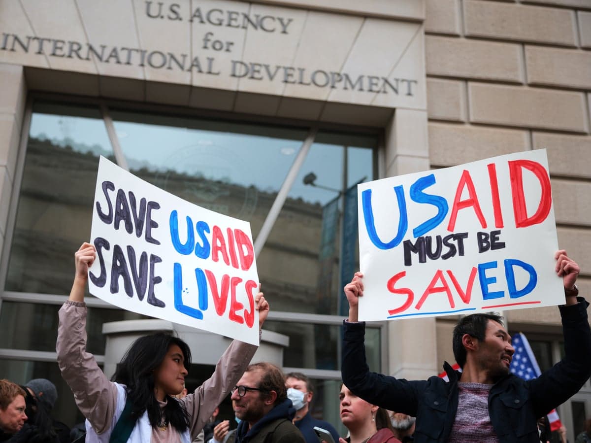Protesters hold handmade signs reading "Save USAID" outside USAID headquarters