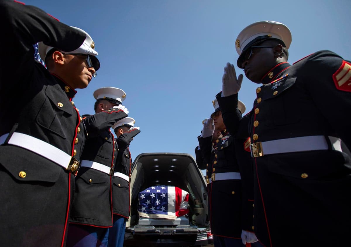 soldiers salute next to a flag draped coffin in a hearse