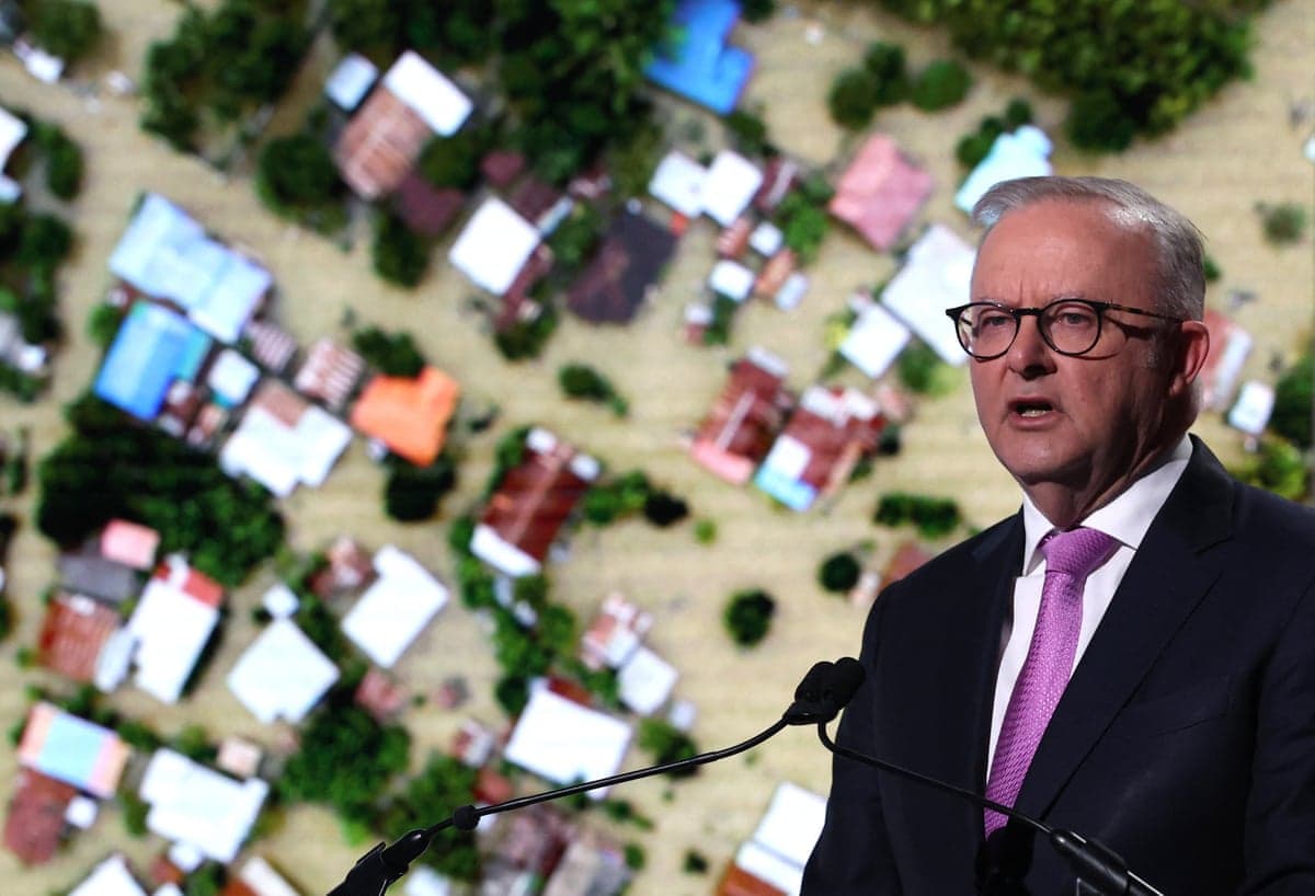 A man in front of a microphone, with an image of a flooded area behind him