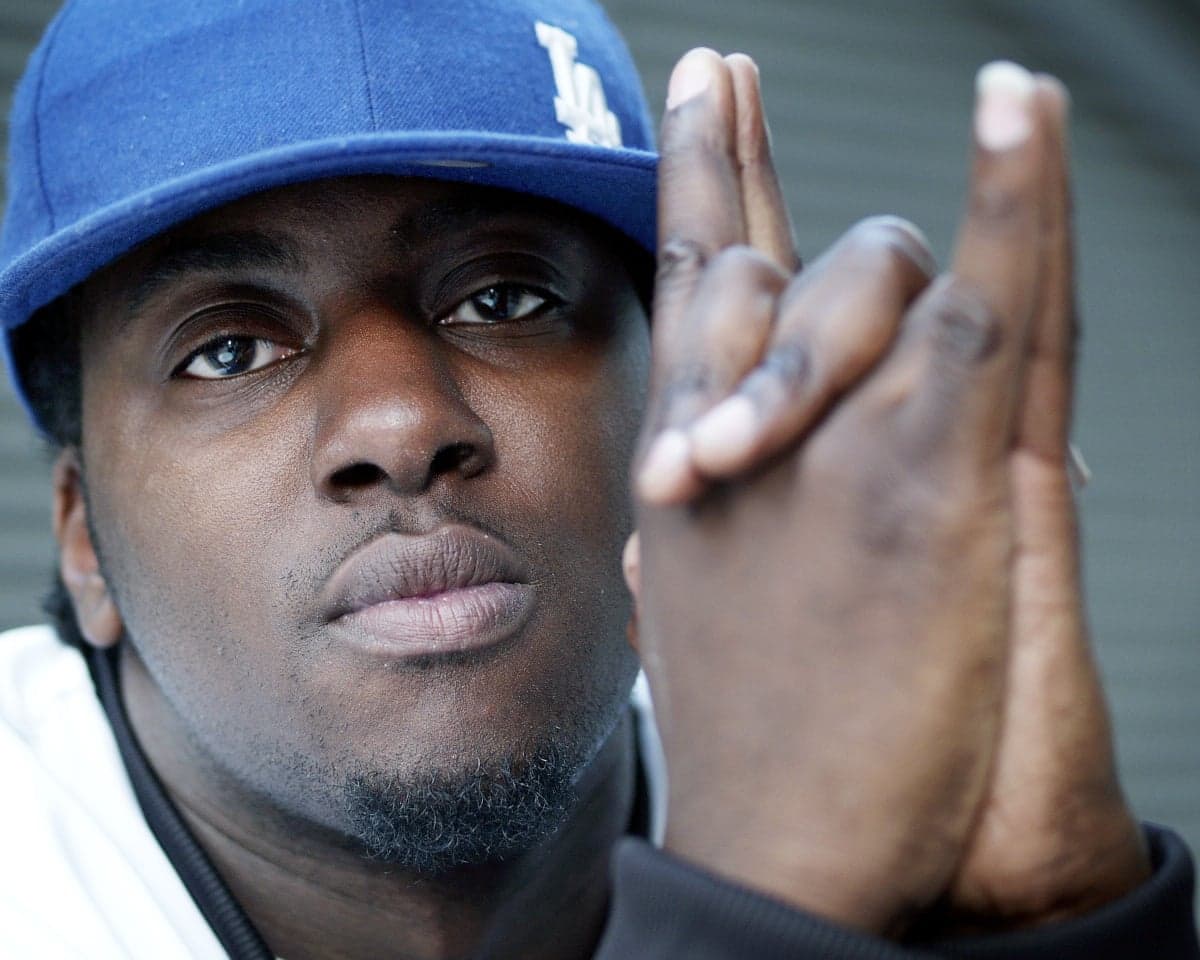 Rapper Sway gestures with both hands, fingers crossed, close to the camera