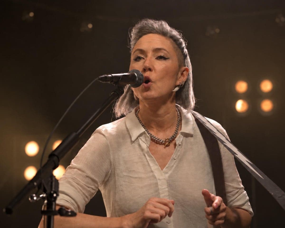 Woman with mid-length hair and white shirt sings into microphone