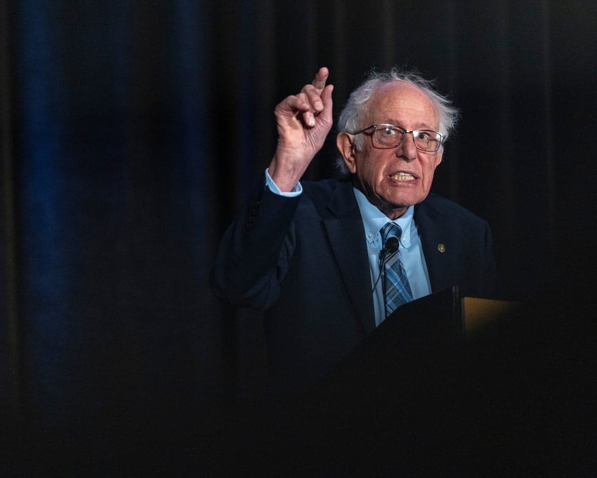 An older man speaks into a microphone and gestures