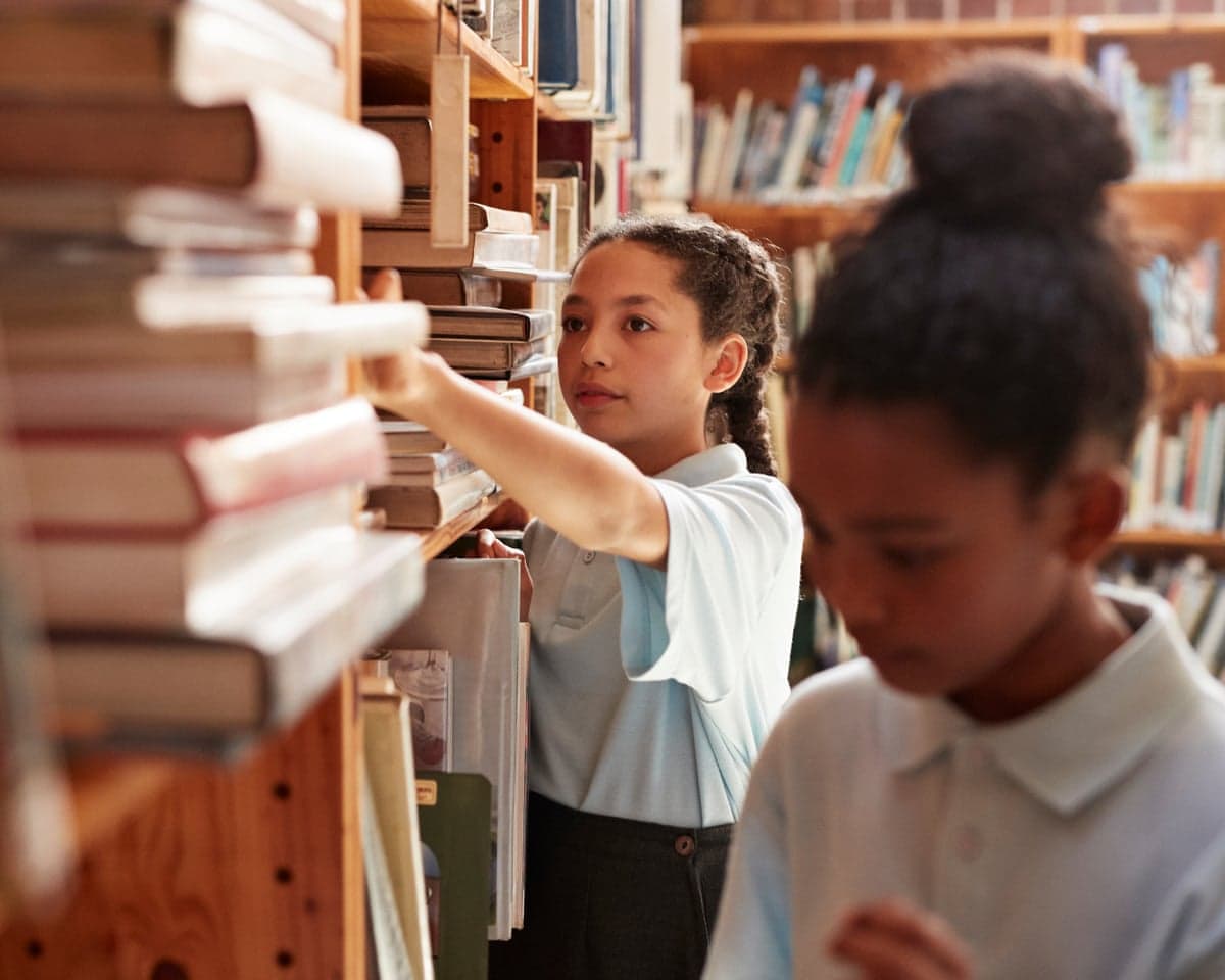 A girl reaches up to a bookshelf in a school library
