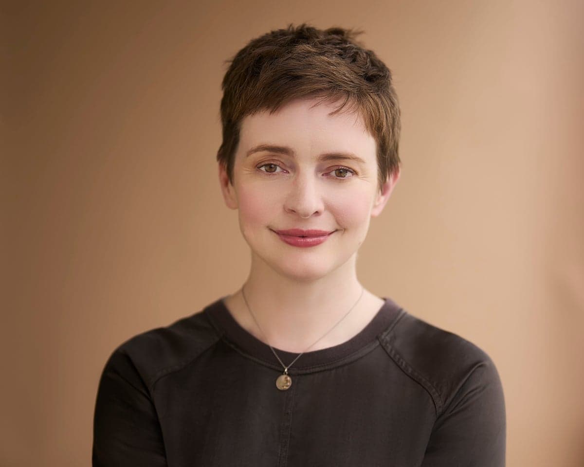 Author Emily St John Mandel, with short brown hair and a necklace, smiles gently