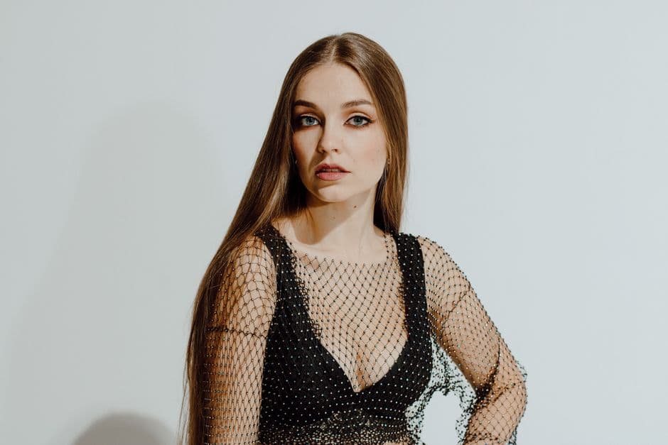 Young woman in fashion mesh top posing confidently in a studio setting.