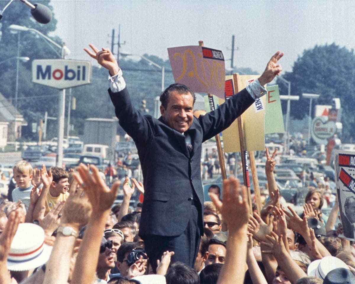 President Nixon raises both arms in a 'V' for victory gesture above a cheering campaign crowd
