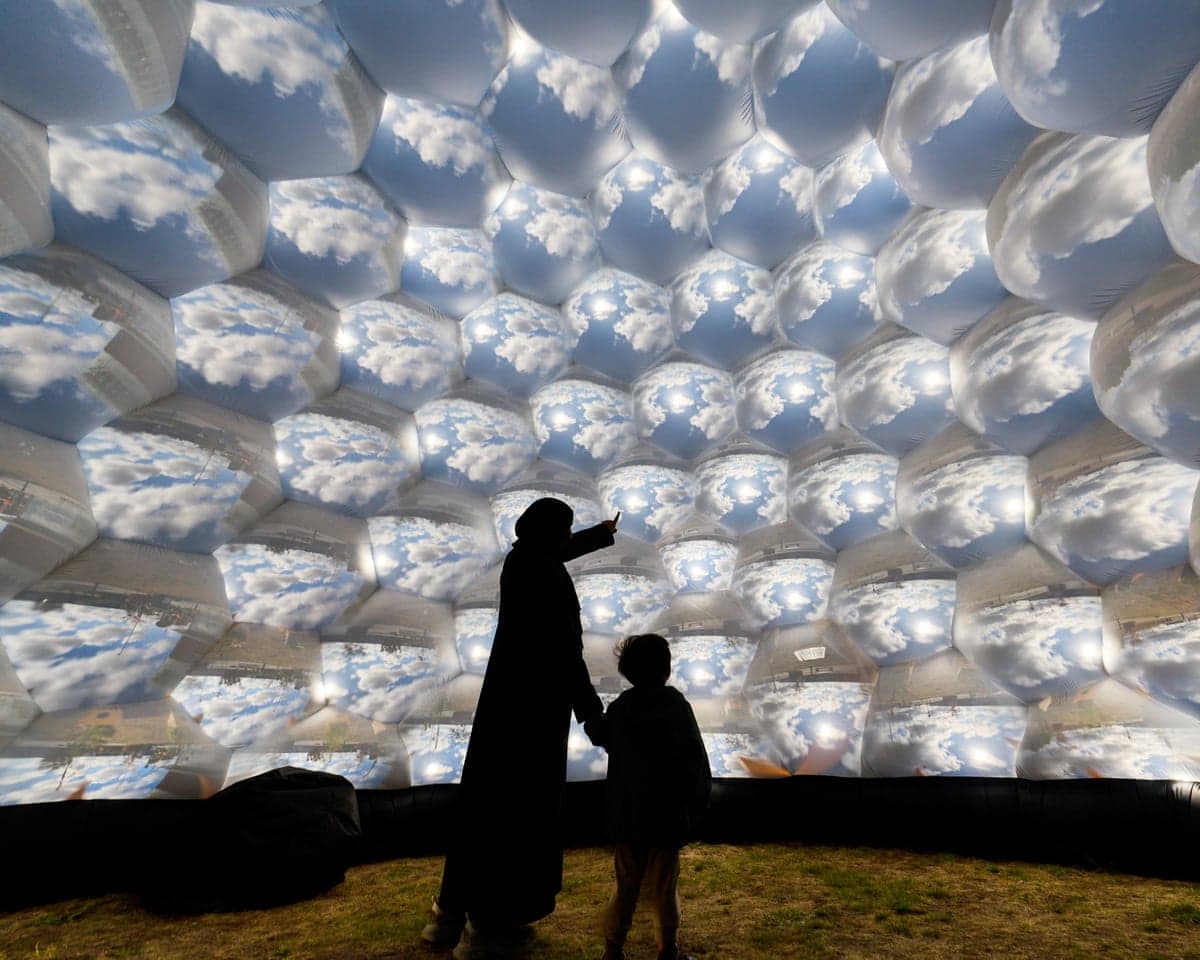 A parent and child inside the Pollenarium standing in front of a 'mosaic' of views of the outside world.