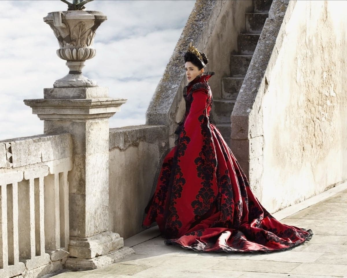 Salma Hayek, in character, wears an ornate red and black gown on a stone staircase landing in Tale of Tales