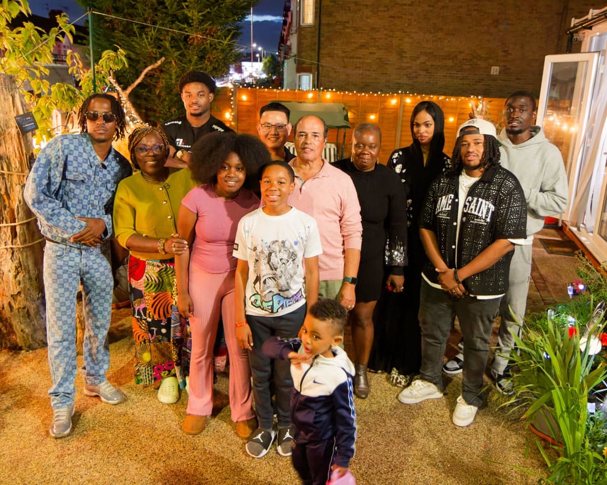 Symon and his family pose together outdoors at night in a garden