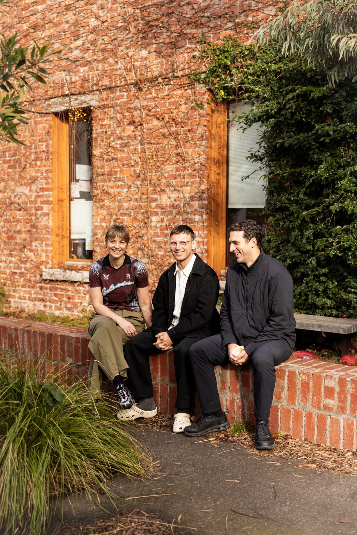 Three people sitting on a low brick wall outside a brick house