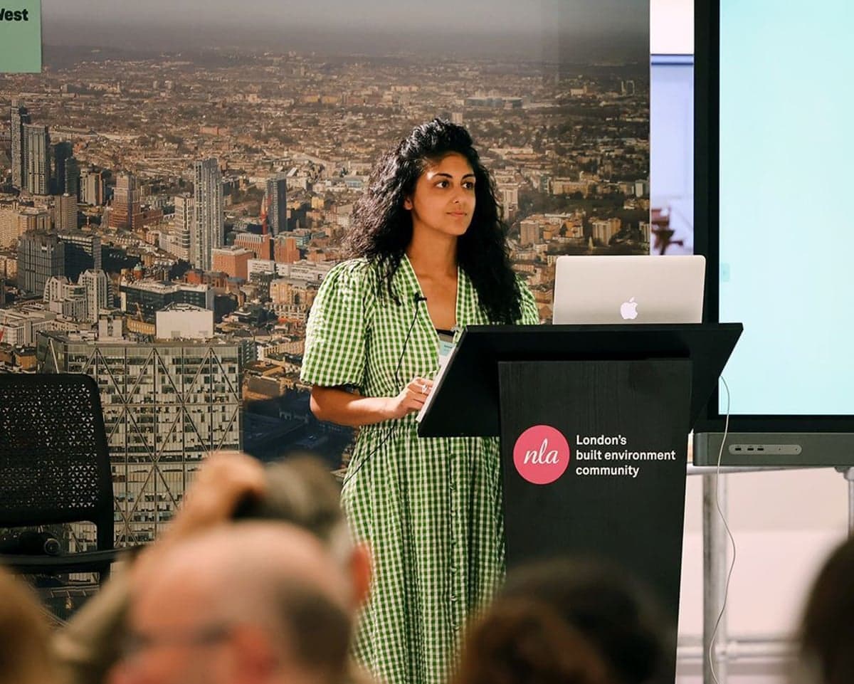 Amanprit Arnold speaks at a podium beside a laptop and projector screen