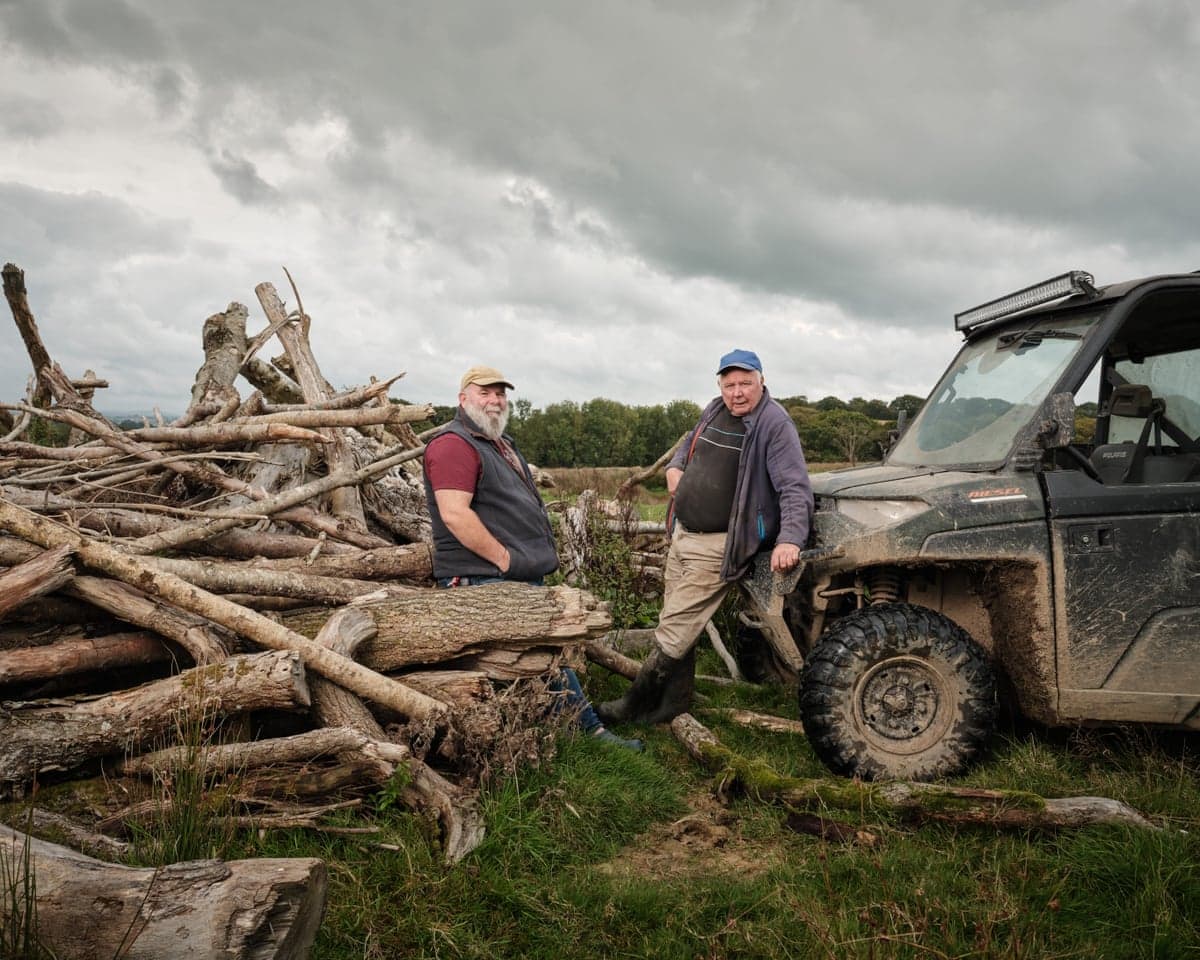 Farmers Derek Gow and Derek Banbury,one leaning against logs, the other a farm vehicle