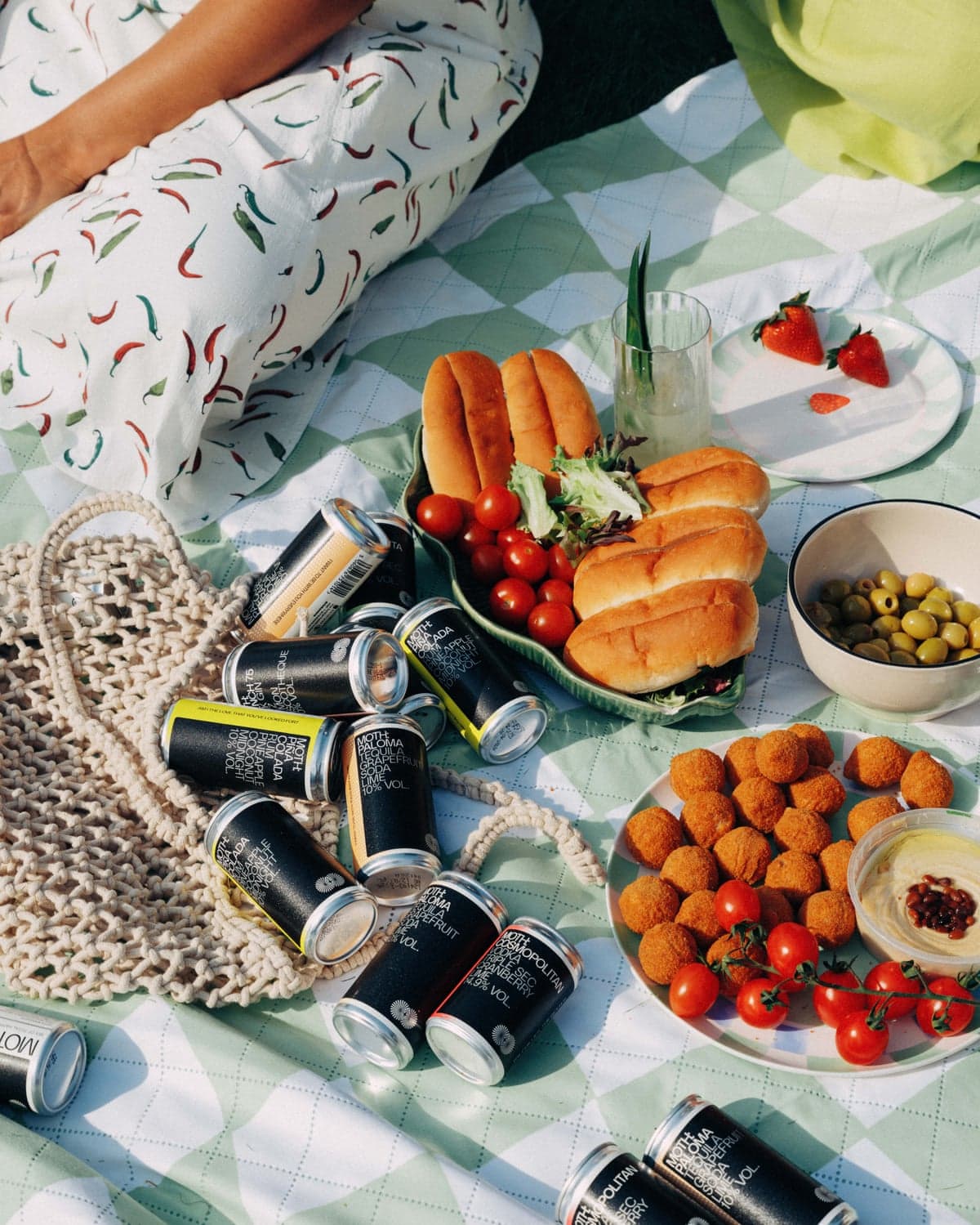 Canned Moth drinks, olives, hot dogs, tomatoes, and appetizers spread on a picnic blanket