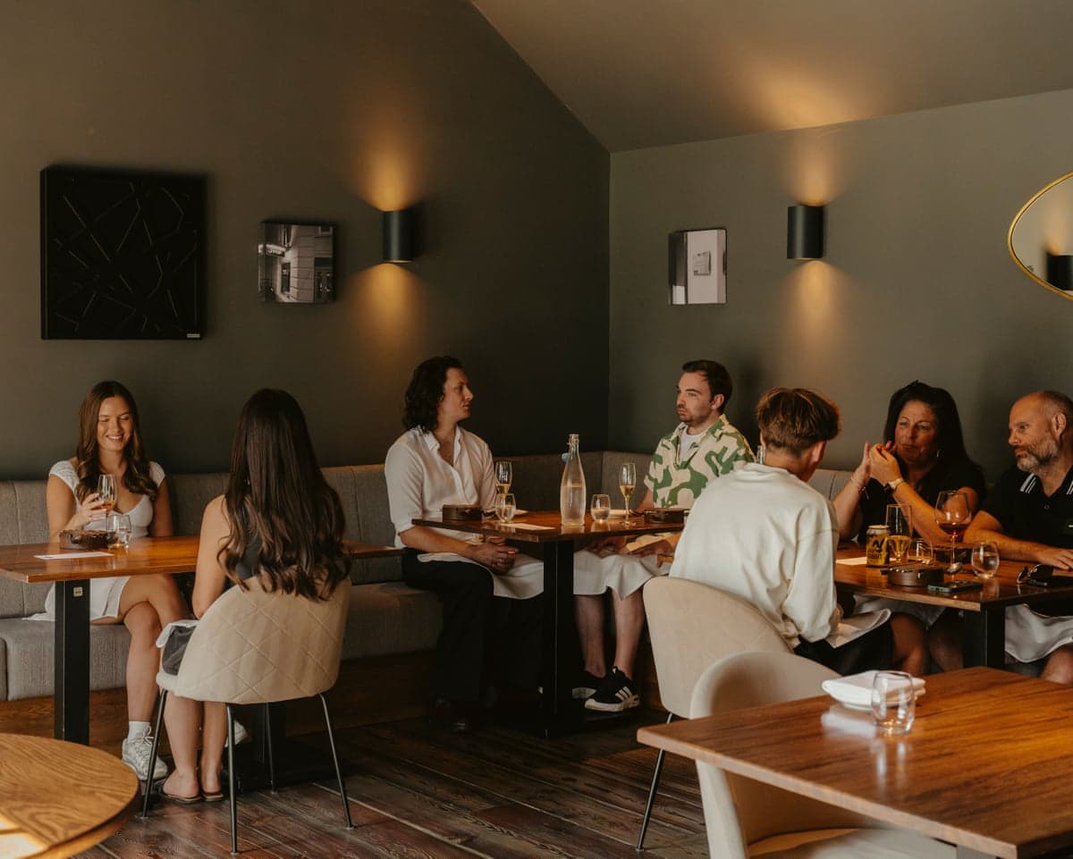 Diners chat around wooden tables in a low-lit room at Kintsu restaurant