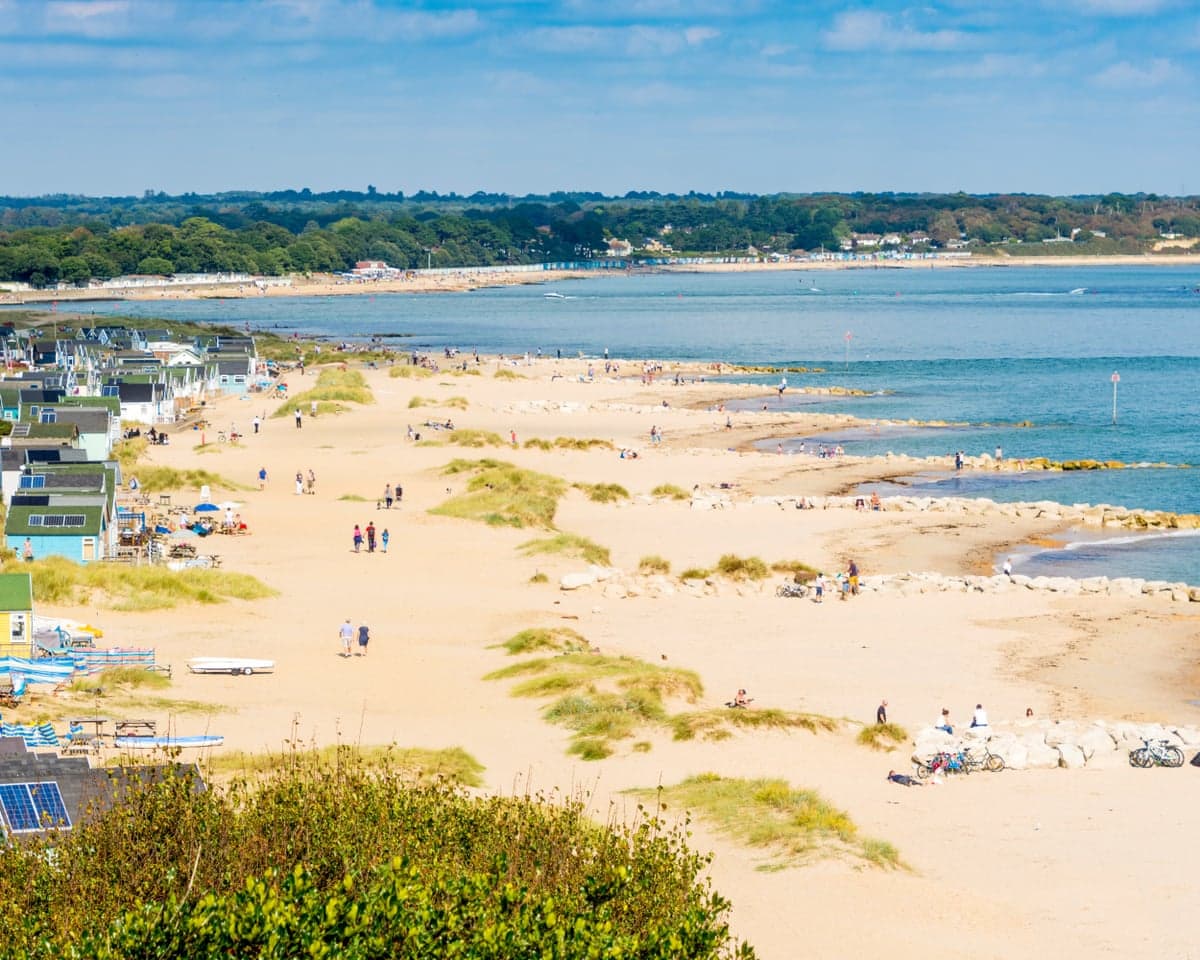 Aerial view of Hengistbury Head beach with dunes, beach huts, and people walking near the sea
