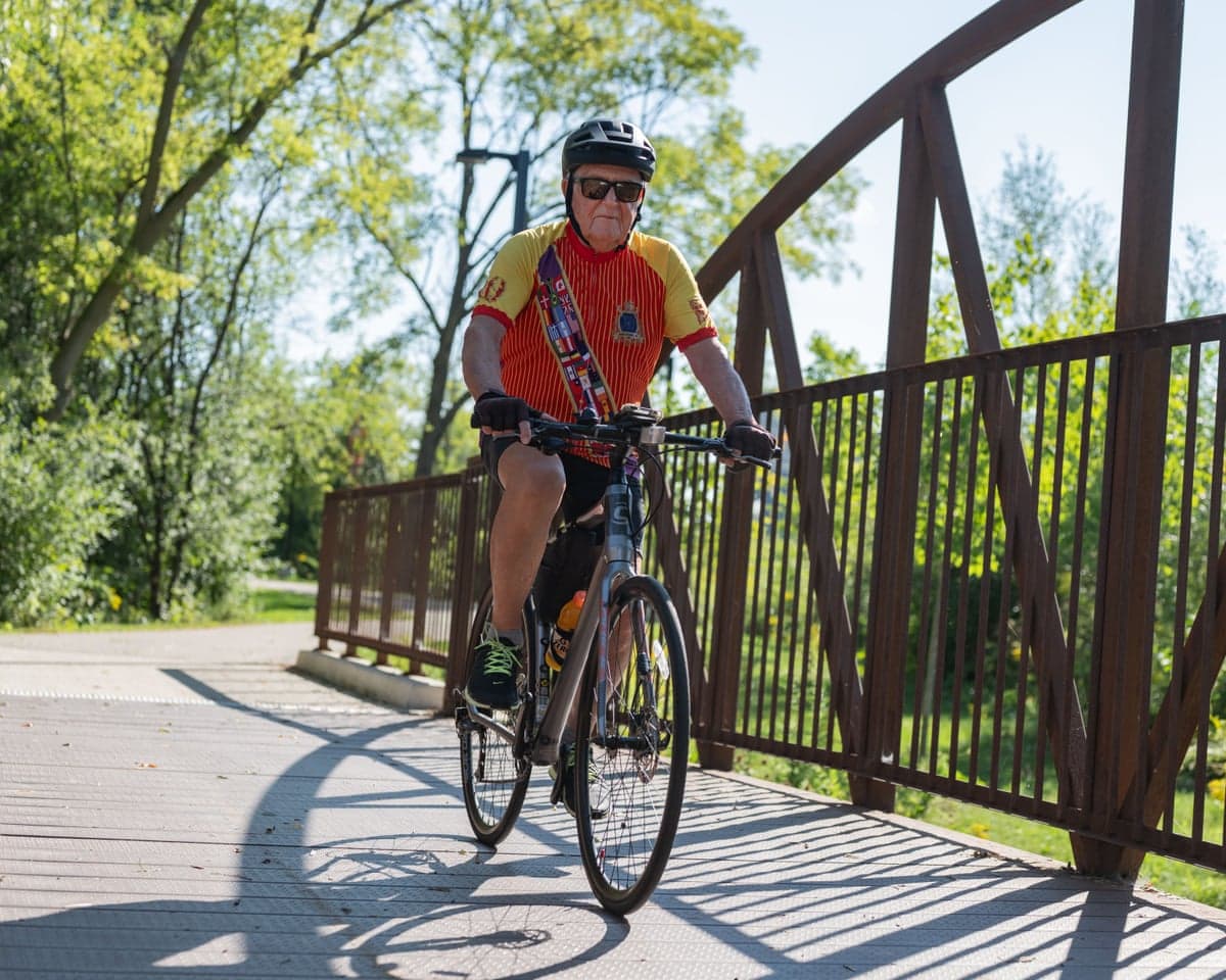 Arthur Plummer, in helmet and cycling jersey, rides a bicycle across a bridge.