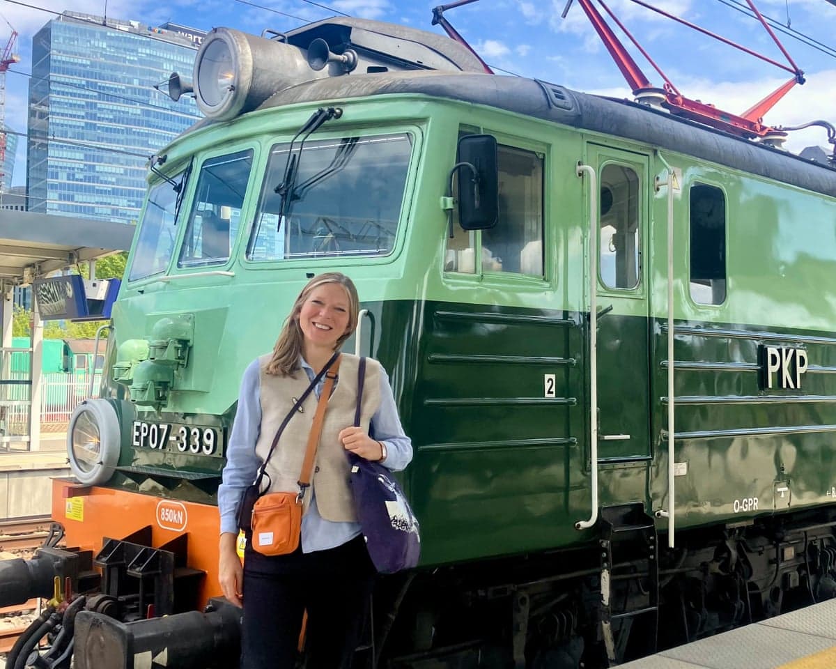 A blond woman standing on a railway platform next to a smart two-tone green train with the lettering PKP