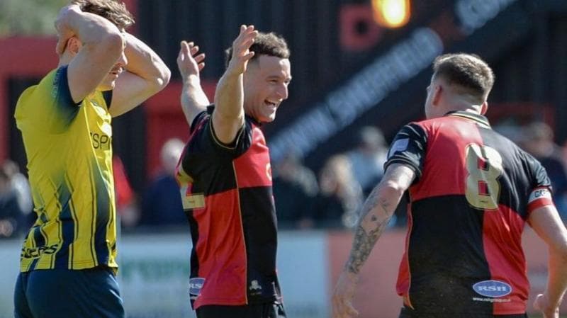 Sheffield FC players celebrate a goal with an opposition player looking dejected in the foreground