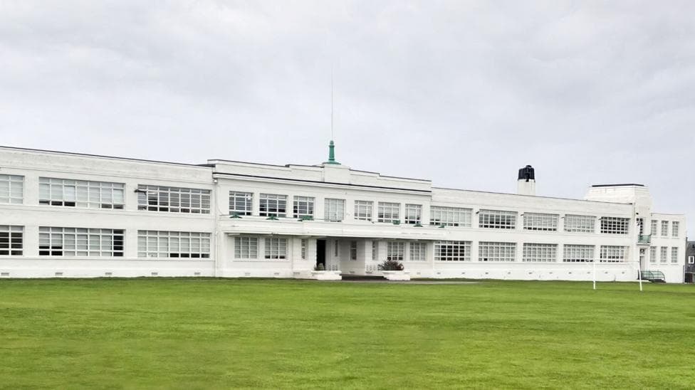 Inverness High School's main building is of a 1930s white walled art deco style with sleek lines, including long windows.