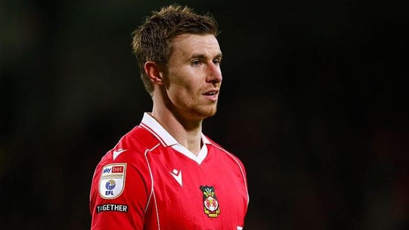 Wrexham midfielder Ben Sheaf in a red Wrexham shirt set against a dark background
