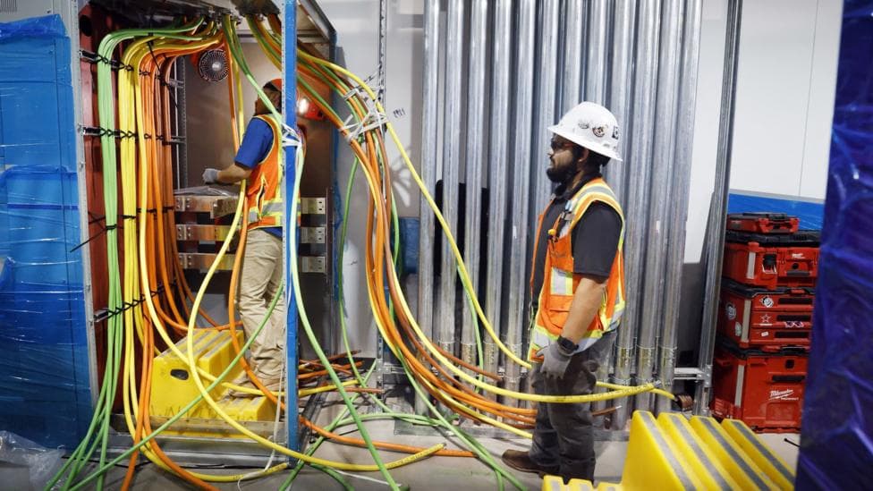 Two workers in hi-vis jackets work with bundles of cabling at a data centre project