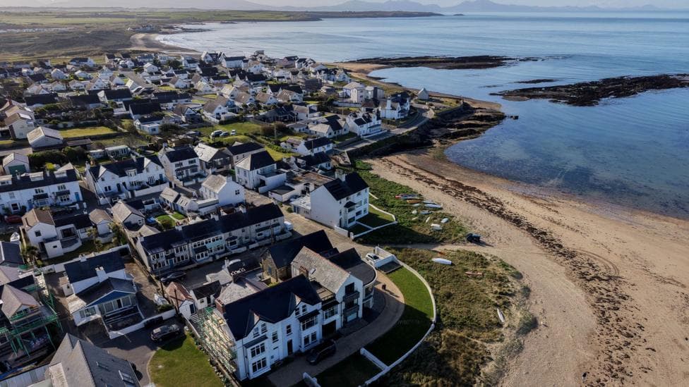 Aerial drone view of Rhosneigr Beach coastline in Anglesey north Wales. It shows a sandy beach, alongside homes.