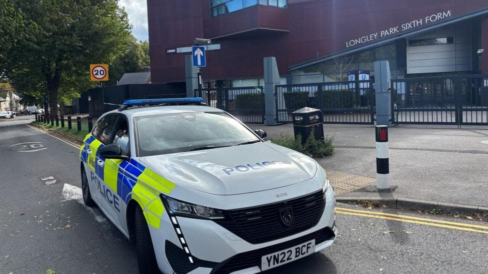 A marked police car parked in the street outside a large building. A sign on the building says Longley Park Sixth Form.