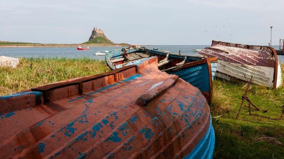 A view across the water to Holy Island with upturned boats on the shore and a view across the water to the island