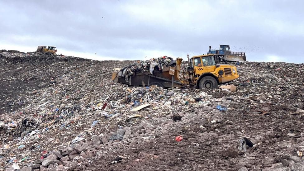 A landfill site with rubbish on the ground and machines pushing it into place.