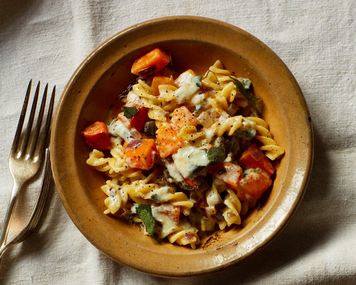 A bowls of fusilli pasta with roasted vegetables, sage, and gorgonzola, beside a fork
