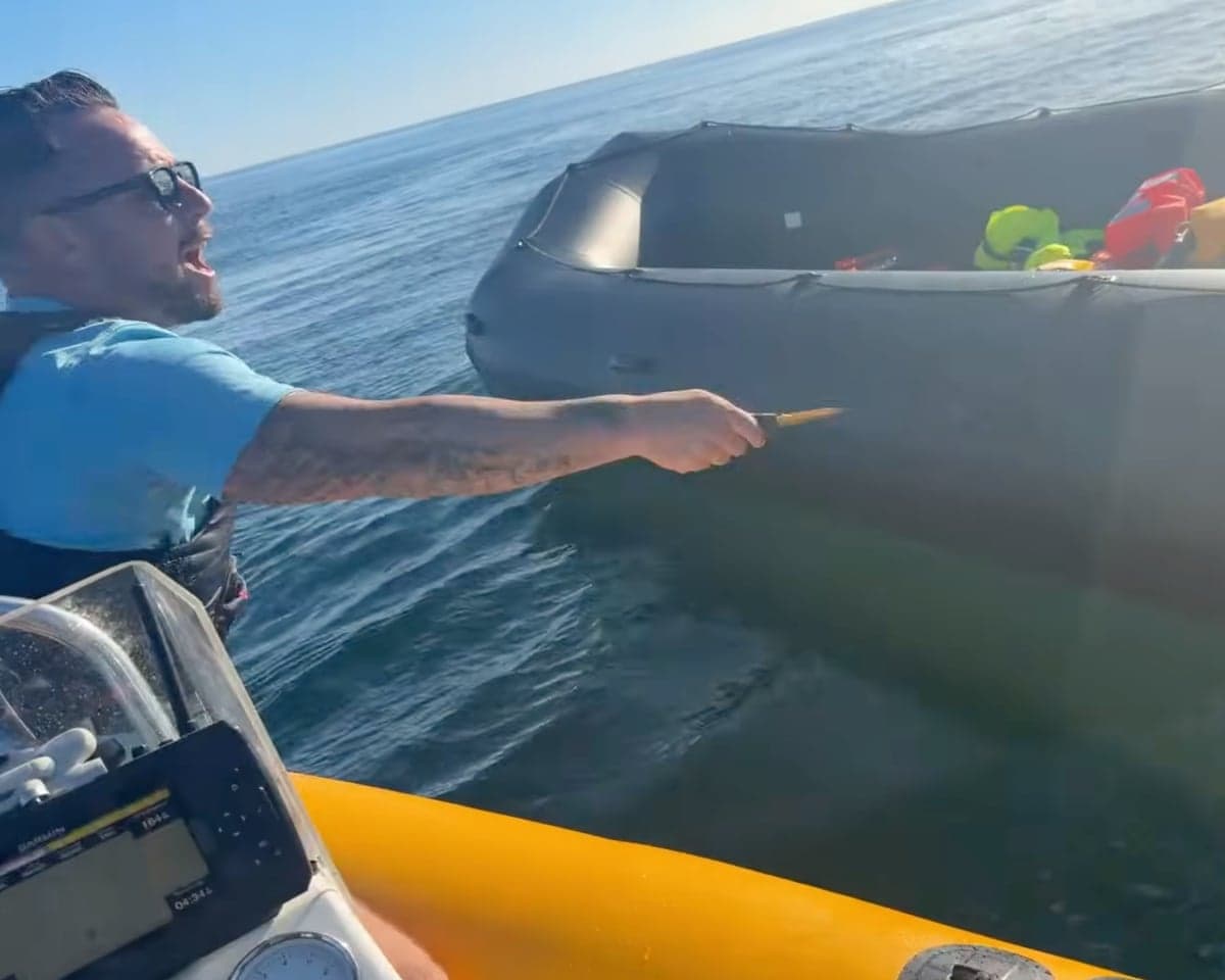 Daniel Thomas shouting from small boat pointing a sharp object at a dinghy at sea.