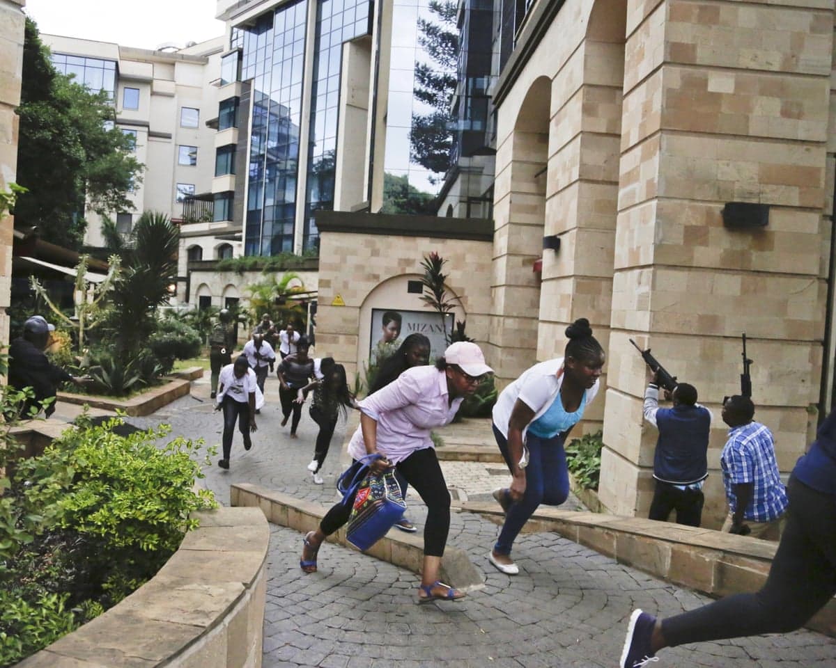 Civilians flee as security forces aim their weapons at a hotel complex