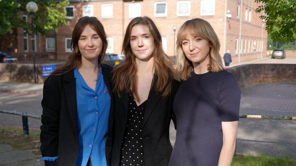 Three woman look towards the camera wearing formal clothing outside a court building.