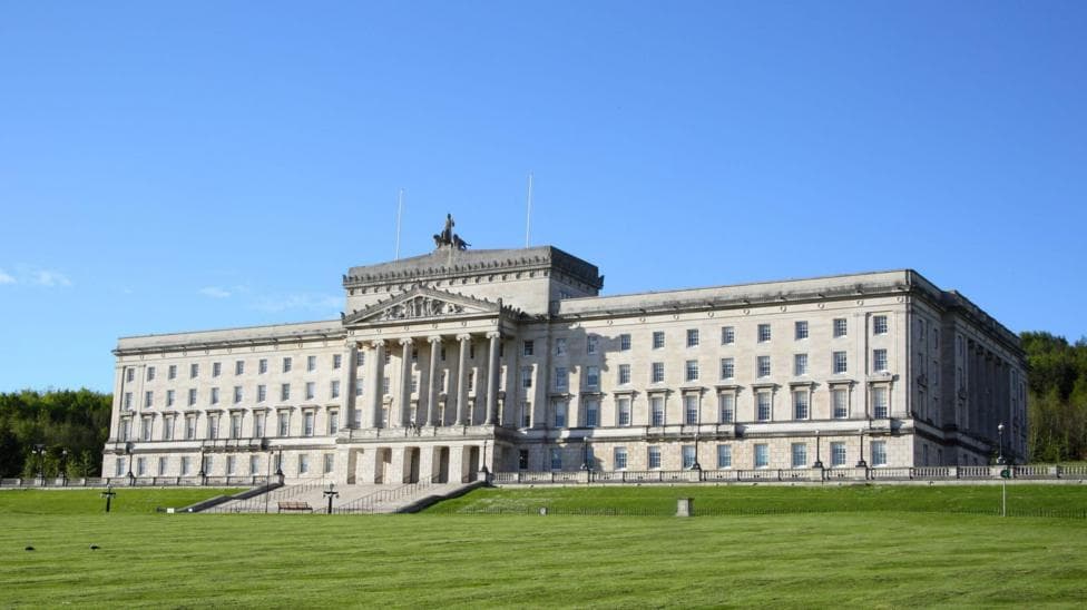 Parliament Buildings at Stormont, a large white stone building with pillars and a lawn in front.