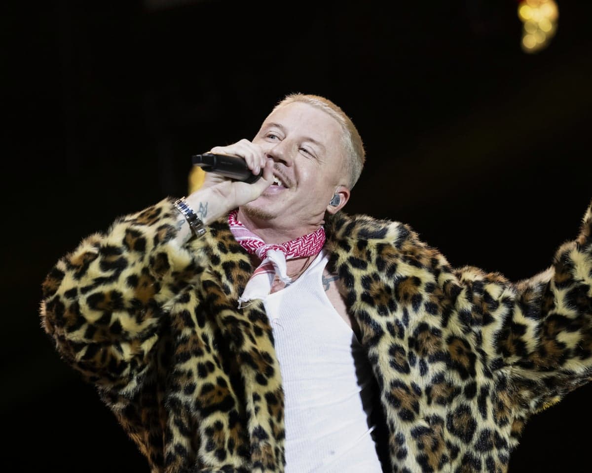 Macklemore performing onstage wearing a furry leopard-print jacket, white vest and red keffiyeh neckerchief