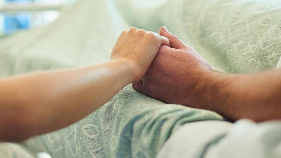 A person holding someone's hand in a hospital bed.