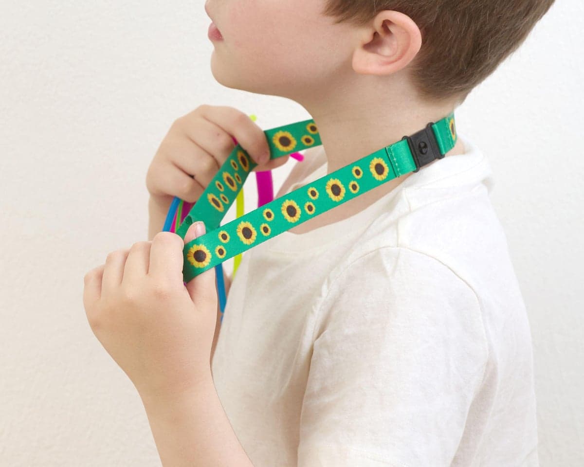 A child adjusts a green sunflower-patterned hidden disability lanyard around their neck
