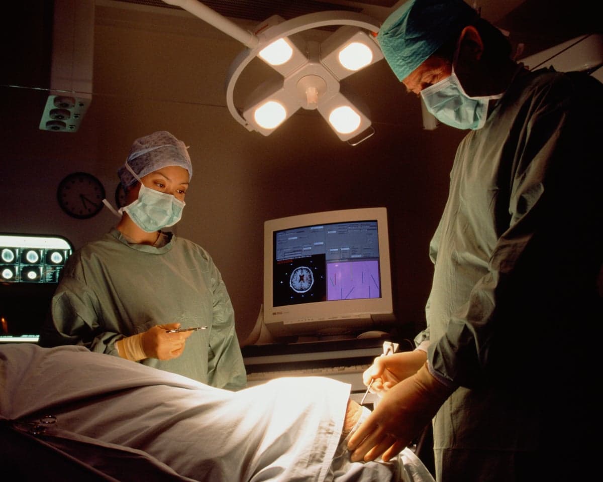 A neurosurgeon and nurse operate on a patient in a hospital operating theatre