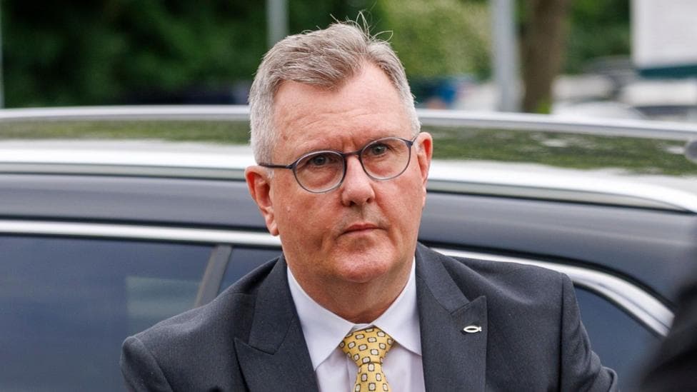 Jeffrey Donaldson. He has short grey hair, wearing a dark grey blazer with a fish pin on the lapel, yellow tie and white shirt.