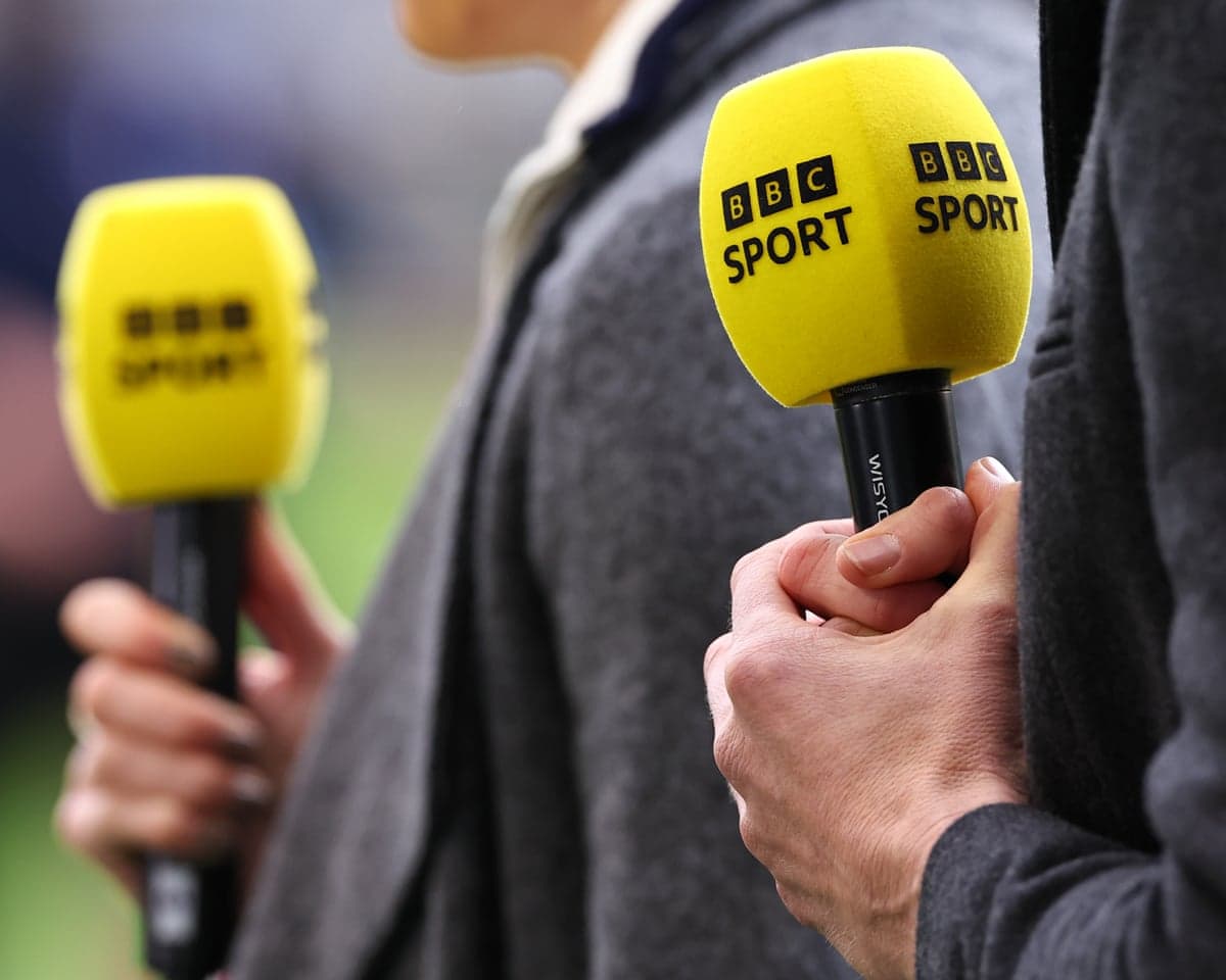 Close-up of yellow BBC Sport branded microphones held by people at a football match