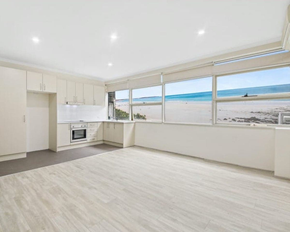 An apartment kitchen with what appears to be Bondi beach out the kitchen window but is actually a mural on an outdoor wall