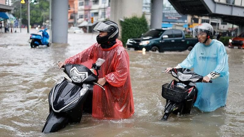Two men pushing scooters through a flooded road in Bangkok