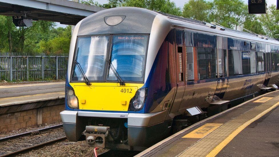 A train parked at a station. It is mostly blue and silver, and has a yellow box ohn the front.