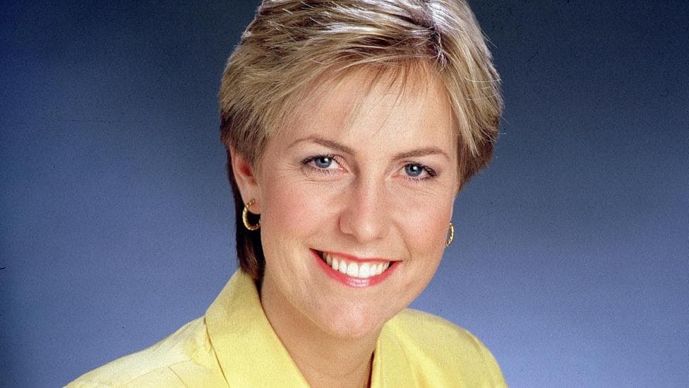 Jill Dando smiles at the camera, wearing a yellow shirt and pink lipstick. She has blue eyes and blonde hair.