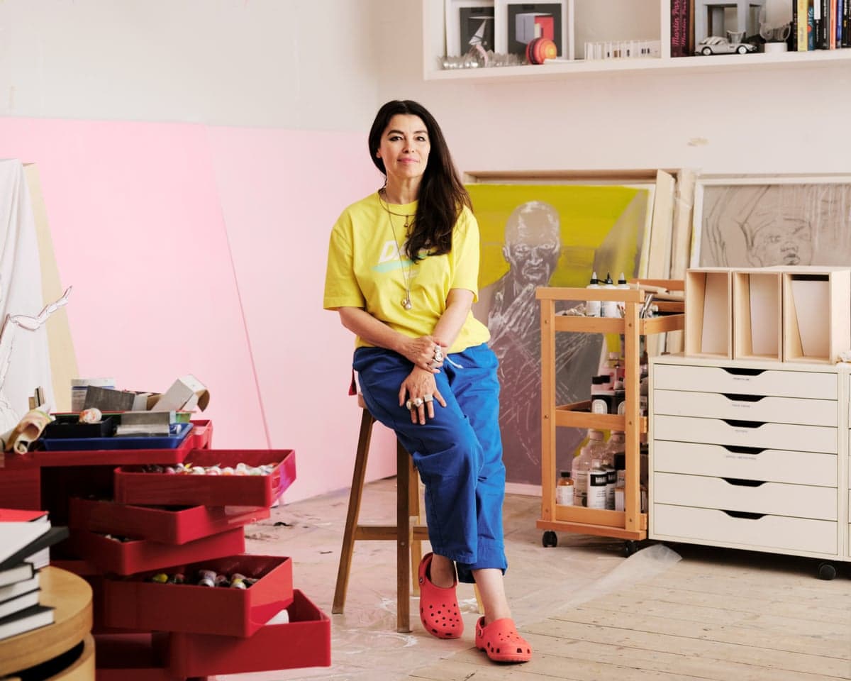 Es Devlin in a yellow T-shirt and blue trousers standing in her studio.