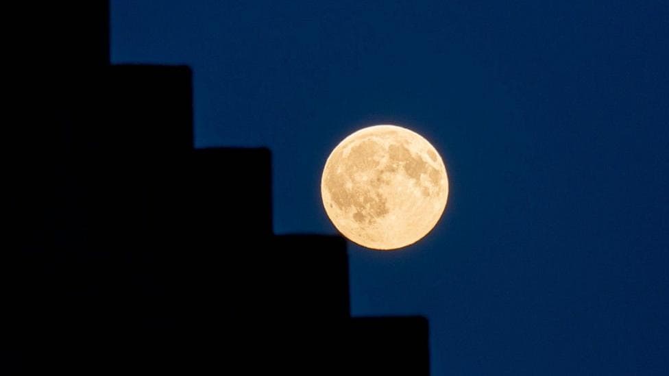 A building is silhouetted to the left to look as if it is black steps and the golden Moon is pictured halfway across creating an illusion that it's rolling down stairs.