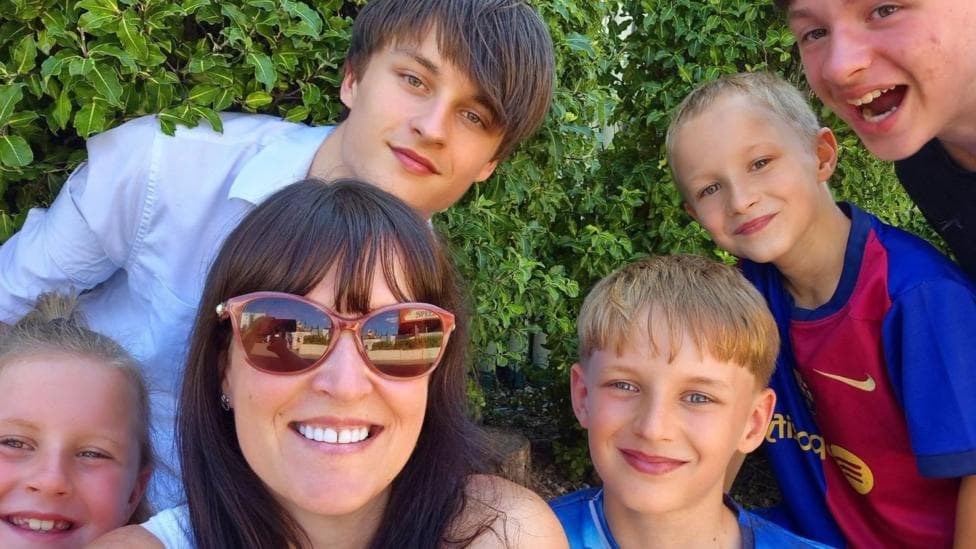 Niaomi Flewers with her four sons and daughter who are all smiling towards the camera. Niaomi is in front and wearing red sunglasses.